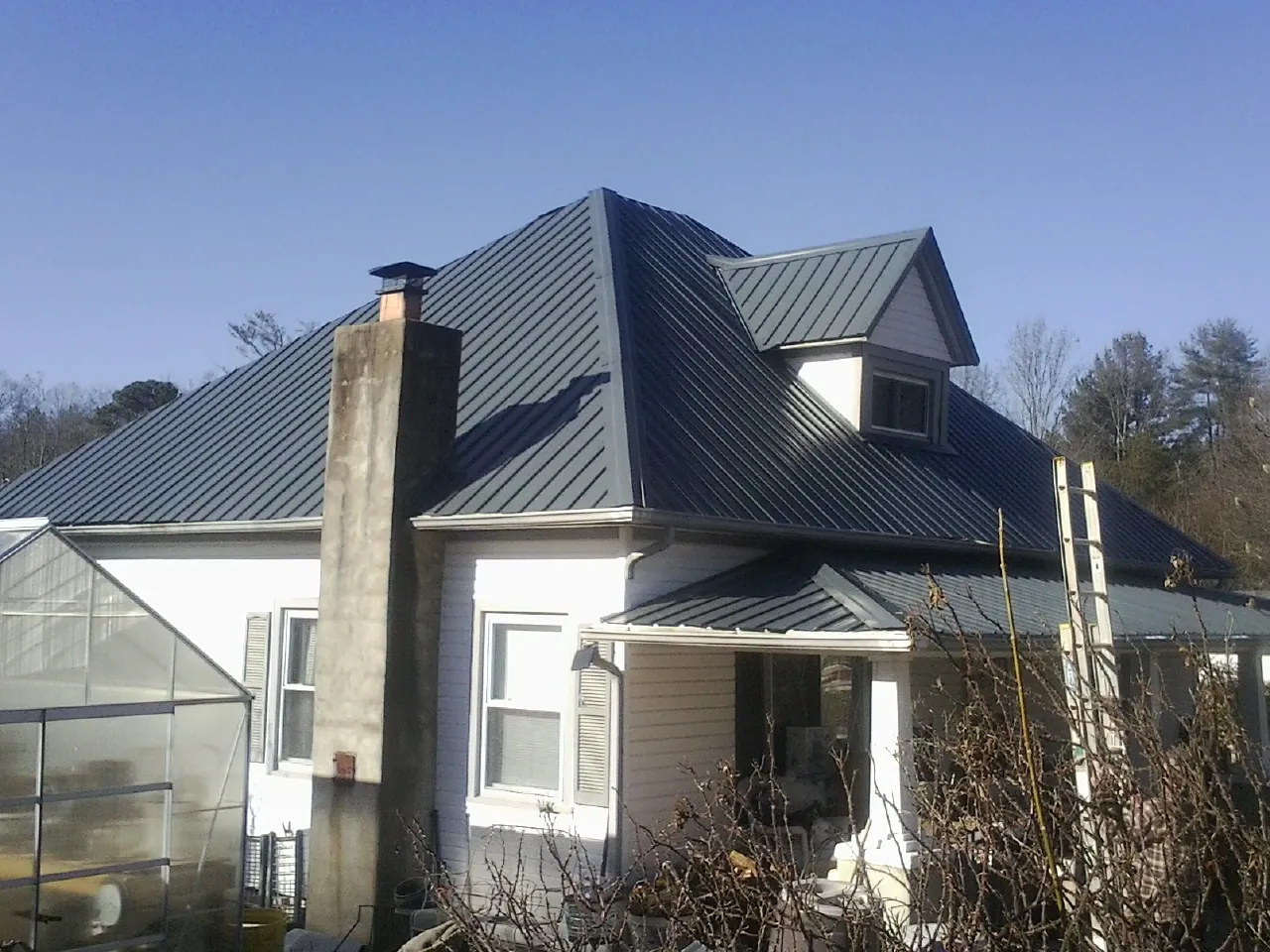 Dark blue standing seam metal roof on a white farmhouse with dormer — Slate & Tile Roof Repair by Roofing Brothers in Whitewater