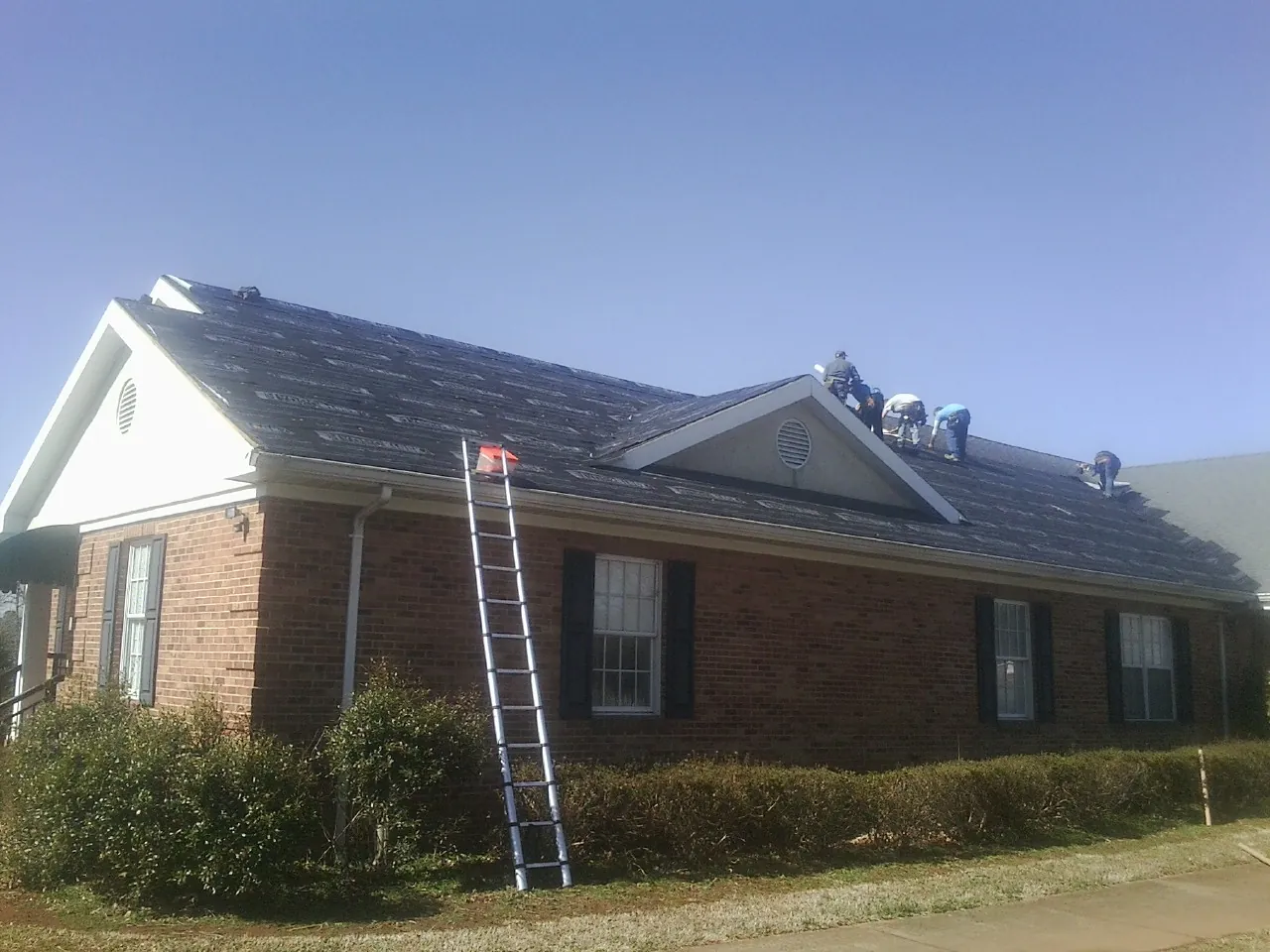 Crew tearing shingles off a brick ranch roof with a ladder set — Emergency Roof Repair work by our crew in Whitewater