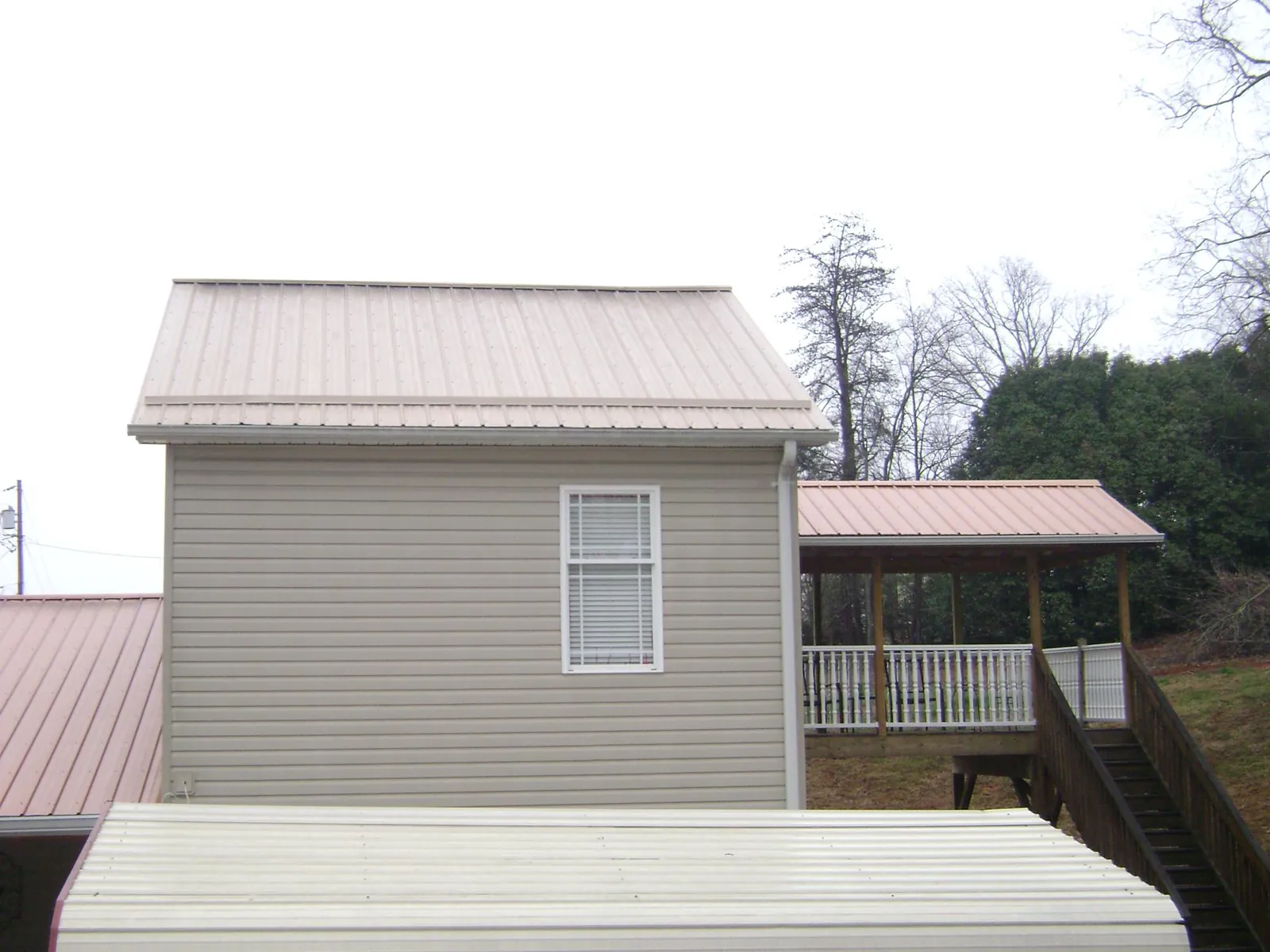 Tan metal roofs on a two story addition and attached porch, from a Roof Replacement job in Whitewater